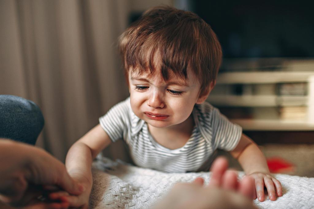 Crying toddler reaching toward parent during an emotional moment